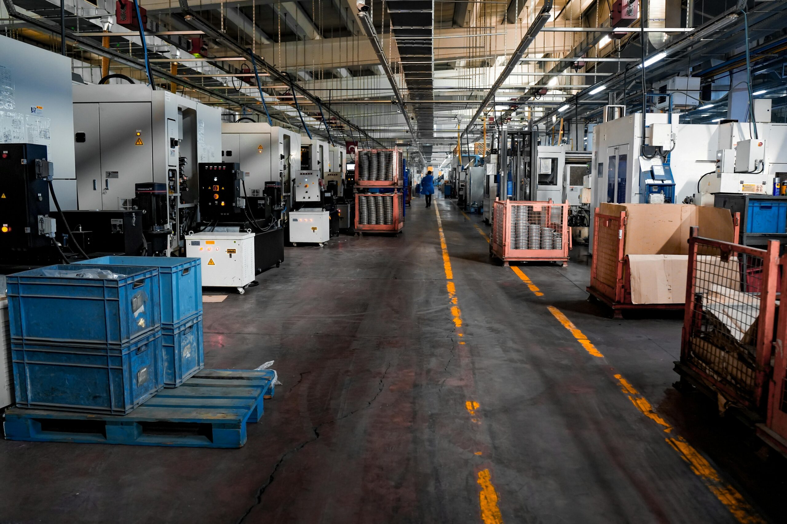 Vast industrial factory floor with machinery, crates, and structured workstations.
